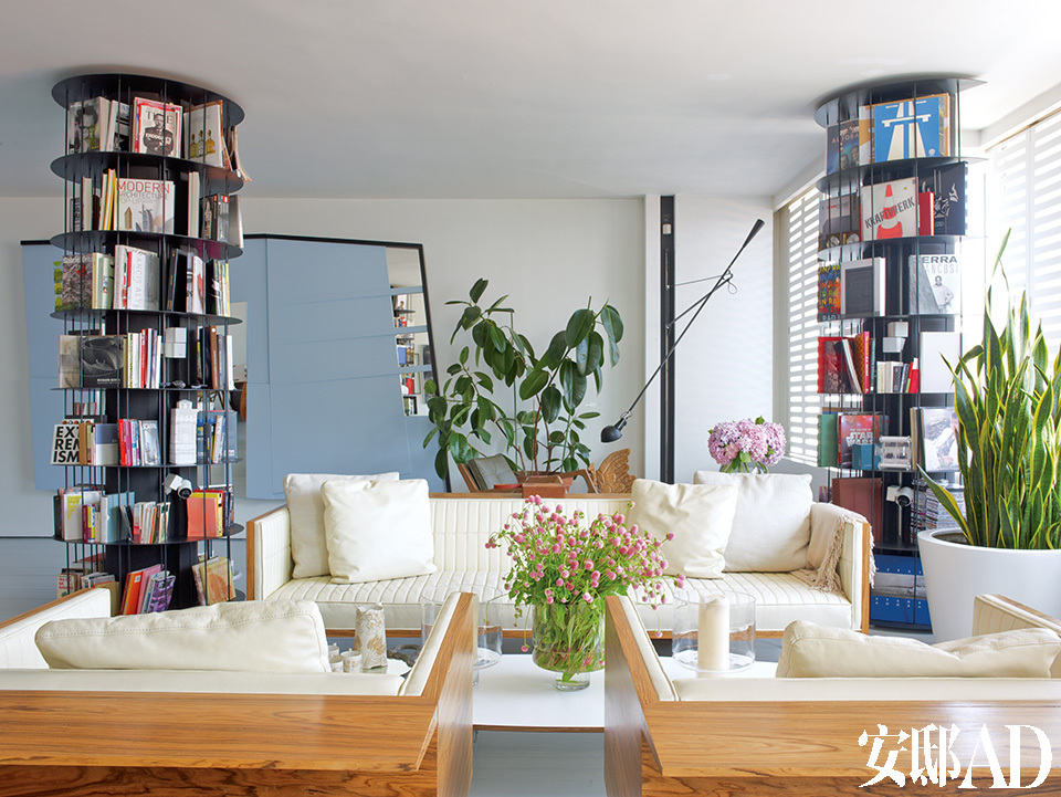 起居室，墙上的蓝色镜面艺术品由Haluk Akakce创作，名为《遗失的空间》（Lostin Space），旋转书架、Box沙发和扶手椅都是由Autoban设计。四只旋转落地书柜将客厅巧妙地分割出不同区域，加之绿色植物的簇拥、美丽光线的环绕，土耳其设计师Sefer Caglar的家是如此明亮舒适、简约而不做作。