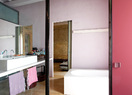 玻璃門反射出的浴室一景。紅色、粉色和湖藍色中和了浴缸硬朗簡潔的線條。