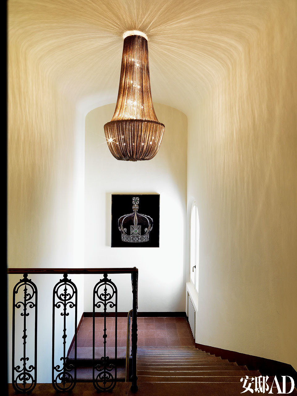 Philippe Montels设计的Galahad金属吊灯华丽地装扮了楼梯间，它在古老的弧形天顶上投射出礼花般的放射状光线。黑底色的艺术品“Crown”由Michael Astolfi创作，以上产品均来自Visionnaire。