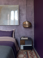 卧室被漆成极富戏剧性的紫色调，带有金属元素的装饰物和艺术品为整个房间增色不少。卧室的墙面被漆成了极富戏剧性的紫色，却仍与地砖上的彩色图案相衬。床上的被单、床头墙面上精致的淡绿色艺术品，都与床头柜的色调巧妙呼应。靠枕、床单、床罩的选择，更是助长了卧室里这种戏剧化的配色效果。